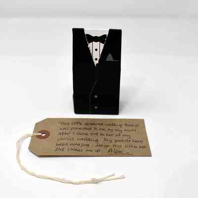 Small black box made out of card, patterned like a tuxedo. There is a small white string coming out of the top right corner of the box.