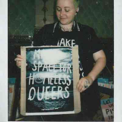 A person holds a poster advocating for "space for homeless queers".