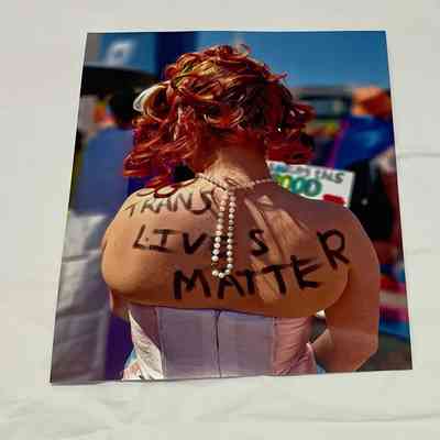The image shows a person from the back wearing a pearl necklace, with "Trans Lives Matter" written across their back.