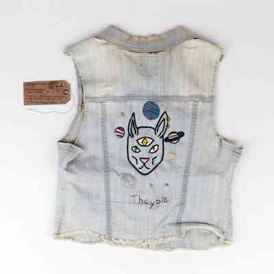 A denim vest displays a colorful embroidered design featuring planets and a unique animal face.