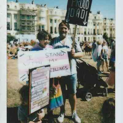 Three people stood holding signs, one of which says 'Proud Dad'.