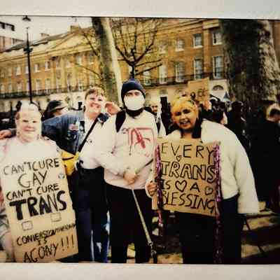 A group of people proudly hold signs which say "CAN'T CURE GAY CAN'T CURE TRANS CONVERSION THERAPY IS AGONY" and "EVERY TRANS IS A BLESSING".