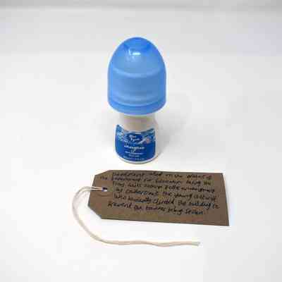 An Insignia brand roll-on deodorant. the bottle is mushroom shaped with a blue lid and a blue label. With a brown, handwritten luggage tag.