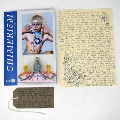 The image shows a book titled "CHIMERISM" alongside a handwritten letter and a small tag.