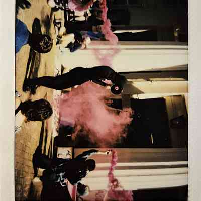 A group of people gather outside a building as pink smoke fills the air.