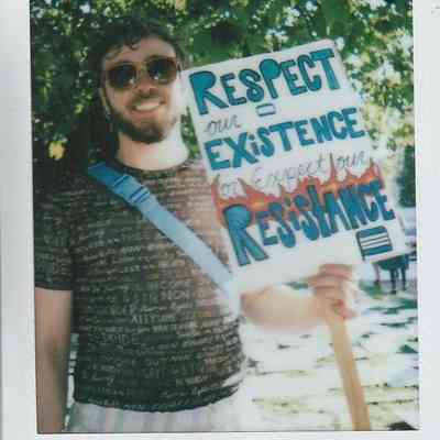 A person wearing sunglasses holds a sign that reads, "Respect our existence or expect our resistance,".