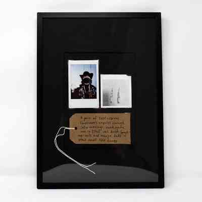 A black-framed collage showcases two Polaroids and a brown luggage tag.