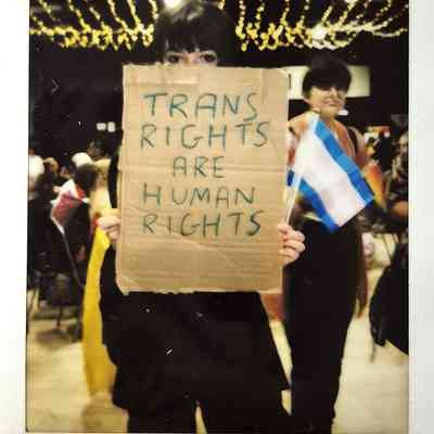 A person holds a sign saying "Trans Rights Are Human Rights" while holding a trans flag.