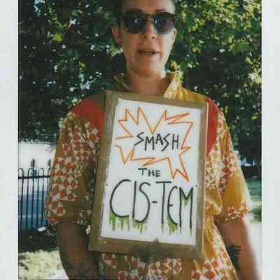 A person wearing sunglasses holds a sign with “Smash the CIS-TEM” written on it.