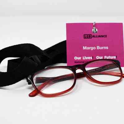 A photograph of a pair of red glasses resting next to a pink name badge which says 'LGB Alliance' with a black lanyard.
