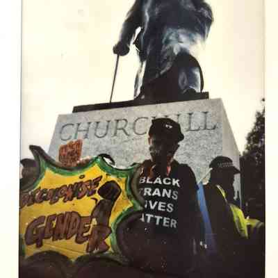 A person stands with a sign and shirt in front of a Churchill statue.