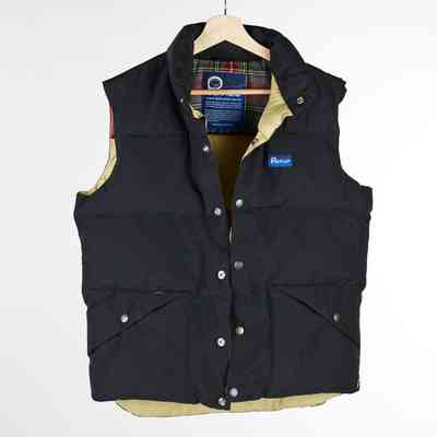 A black Penfield gilet with a cream and tartan lining and poppers down the front and on the pockets on a wooden hangar.