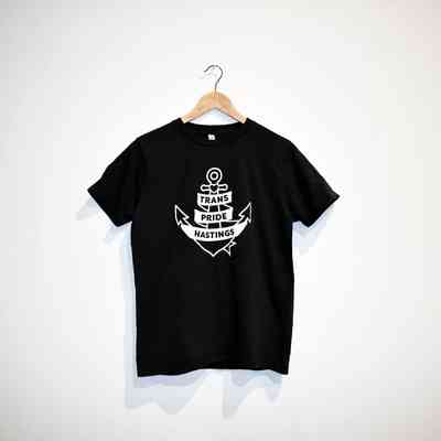 A black T-shirt with "Trans Pride Hastings" is hanging on a wooden hanger.
