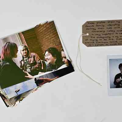 A set of photographs which are lay on top of each other so just on is visible which shows a group of people talking and laughing. The photographs are next to a luggage tag with writing on it and under that a polaroid of a person (the donor) holding the photographs.
