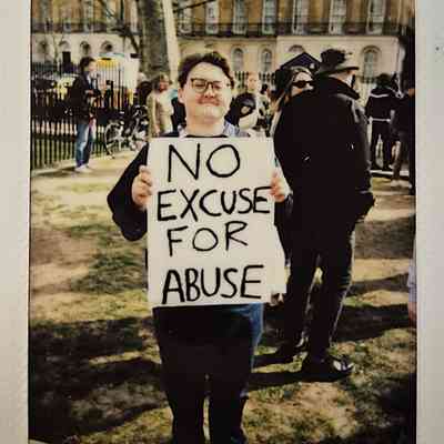 A person holds a sign stating "No Excuse for Abuse" at an outdoor gathering.