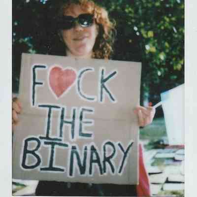 A person wearing sunglasses is holding a sign reading "F❤️CK THE BINARY".
