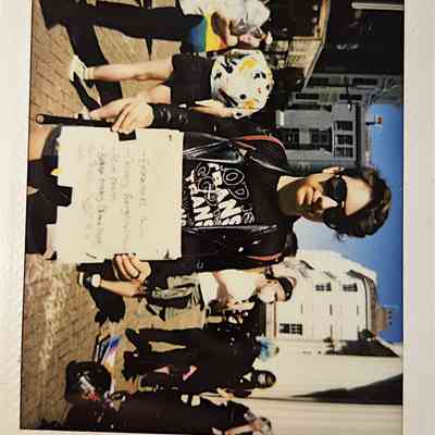 A person in sunglasses holds a handwritten sign during a sunny outdoor gathering with several people.