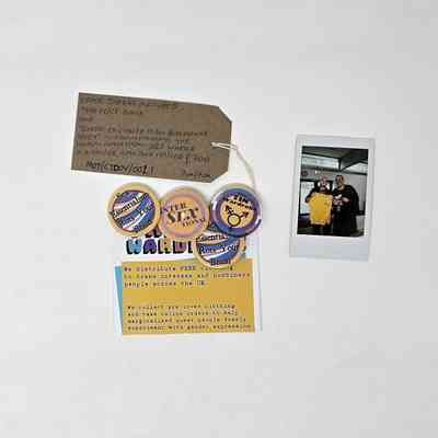Four Badges Pinned Onto 'The Tin Wardrobe' Card. The badges are all in yellow, blues and purples and are of 'Sex Essentialism Rots Your Brain' x2, 'Inter SEX Tional', 'The Tin Wardrobe'.