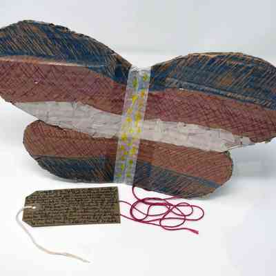 A pair of handmade cardboard fairy wings. They are coloured in blue, white and pink. With some red string and a brown, handwritten luggage tag.