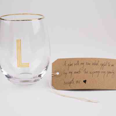 A small drinking glass with a gold rim and the letter "L" in gold. With a brown, handwritten luggage tag.