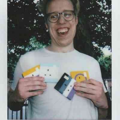 A person wearing glasses smiles broadly while holding colorful plug sockets outdoors.