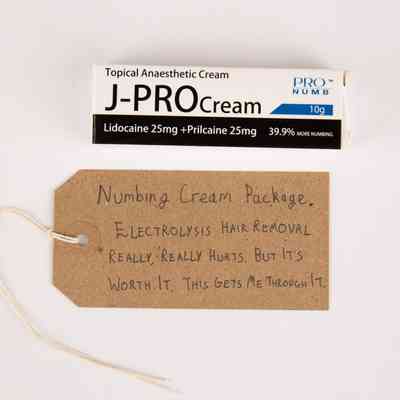 White, black and blue Box of J-PRO topical anesthetic cream. With a brown, handwritten luggage tag.