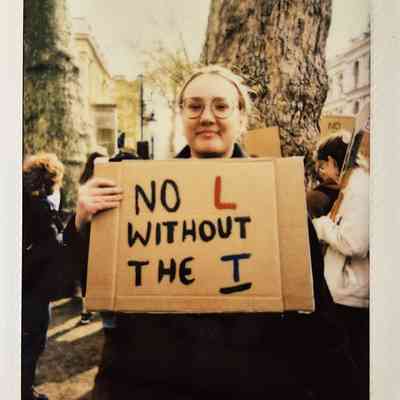 A person is holding a sign that says "No L without the T" in a protest.
