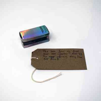 An empty hormone box which is holographic and a brown tag with writing on it next to it.