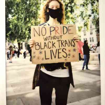 A person stands holding a sign reading "NO PRIDE WITHOUT BLACK TRANS LIVES".