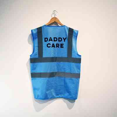A blue safety vest with "DADDY CARE" hangs on a wooden hanger.