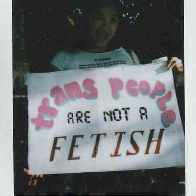 A person holds a sign stating, "Trans people are not a fetish," in the photograph.