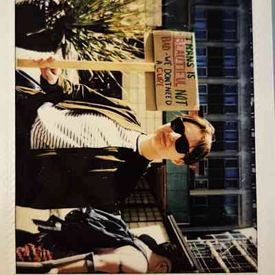 A person wearing sunglasses holds a sign stating "Trans is beautiful".