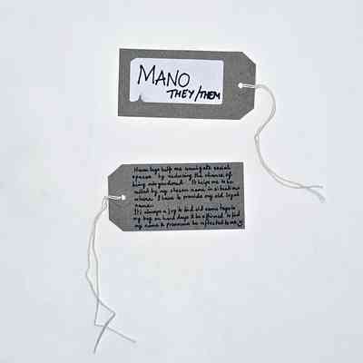 A handwritten name tag inscribed "MANO" "THEY/THEM". With a brown handwritten luggage tag.