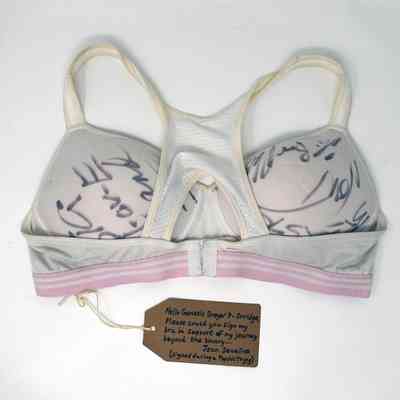 White sports bra with pink bank and various signatures written on the cups in ink.