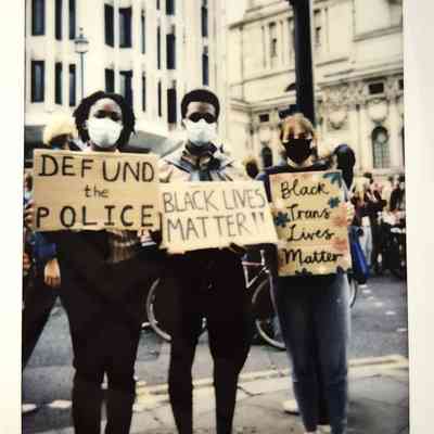 Three masked individuals hold protest signs supporting Black Lives Matter, standing outside.