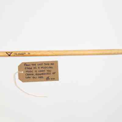 A drumstick with some small writing on it next to a brown tag with writing.