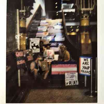 A group of people hold signs supporting LGBTQ rights, in front of an ornate staircase.