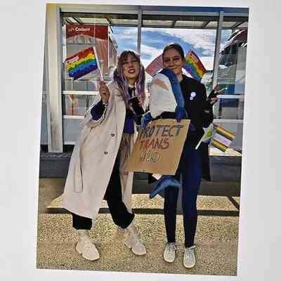 Photograph Showing Two People, One Holding A "PROTECT TRANS KIDS" Sign.