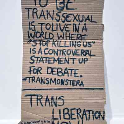 A placard which is made from cardboard and in black marker pen says 'To Be Transsexual Is To Live In A World Where "Stop Killing Us" Is A Controversal Statement Up For Debate. Trans Monstera'