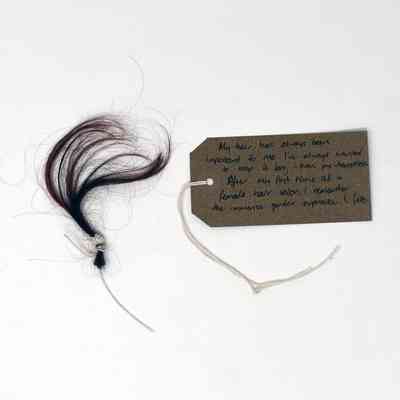 A small tuft of tied dark hair lies next to a handwritten tag on a string.