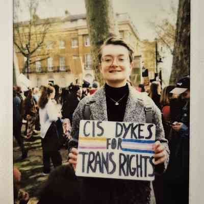 A person smiles while holding a sign which says "CIS DYKES FOR TRANS RIGHTS".