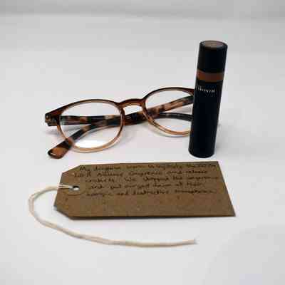 A pair of tortoiseshell glasses, a Rimmel lipstick and a brown, handwritten luggage tag.