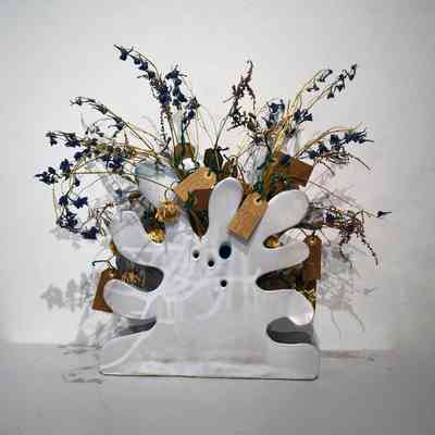 A splatter or blob shaped white ceramic vase holding dried flowers with brown, handwritten tags.