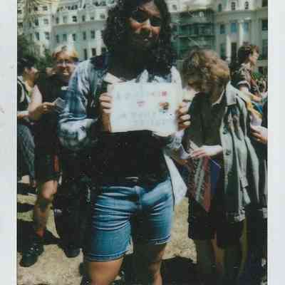 A person stands outdoors holding a sign while surrounded by others during a protest.