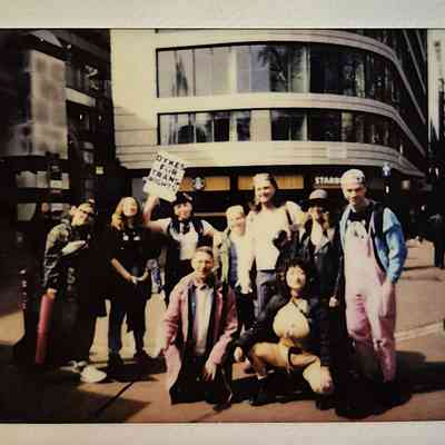 A group poses together on a city street, holding a sign supporting trans rights.