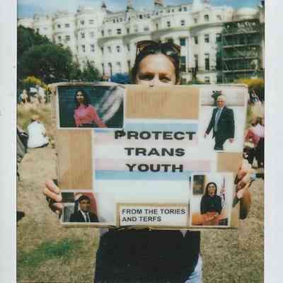 A person holds a sign which says "PROTECT TRANS YOUTH FROM THE TORIES AND TERFS".