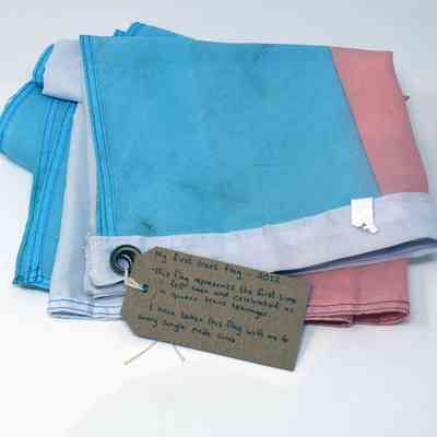 A slightly dirty from use folded up trans flag with a brown tag with writing on it attached.