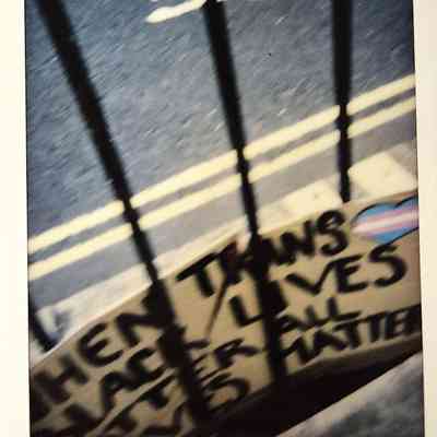 A blurry photo shows a street with signs and a trans flag heart, alongside “BTLM London".