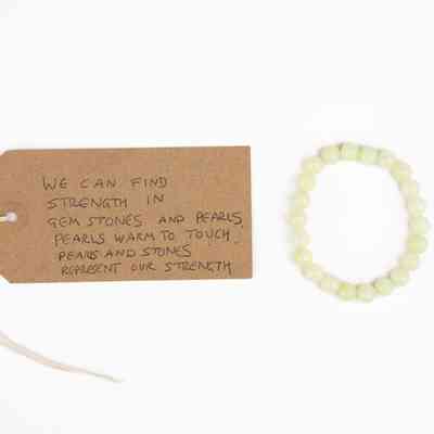 A pearlescent coloured pearl bracelet. With a brown, handwritten luggage tag
