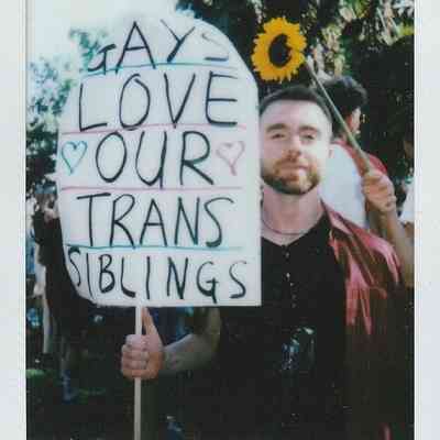 A person at a rally holds a sign saying "GAYS LOVE OUR TRANS SIBLINGS".